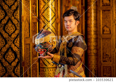 Asian man with traditional cloths relate to Khon or Thai classic masked stand with holding mask Asian man with traditional cloths relate to Khon or Thai classic masked stand with holding mask 103530621