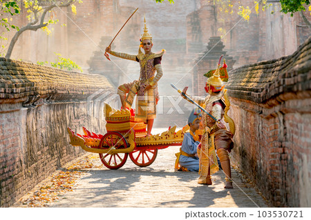 Asian man with old Thai traditional cloth hold weapon and stand and action of dance on chariot Asian man with old Thai traditional cloth hold weapon and stand and action of dance on chariot 103530721