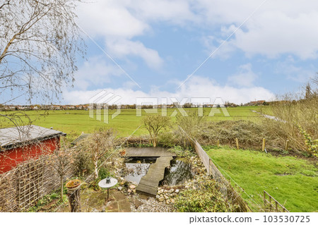 an old red shed in the middle of a green field, with trees and grass on either side there is a blue sky 103530725