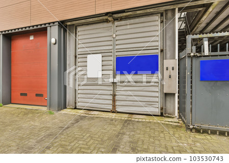 an industrial building with red and blue doors on either side of the building there is a brick sidewalk in front of it 103530743
