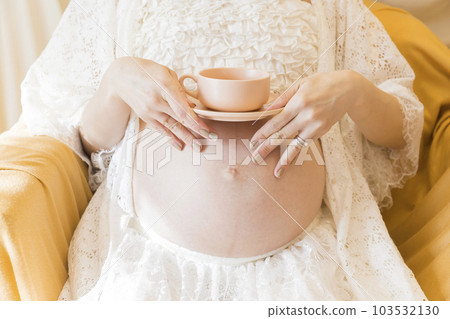 A pregnant woman who is about to give birth and drinks tea while placing a teacup on her belly Premature mother 103532130