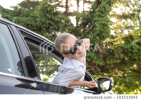A cute boy climbed out of the car window wearing sunglasses and laughing 103533943
