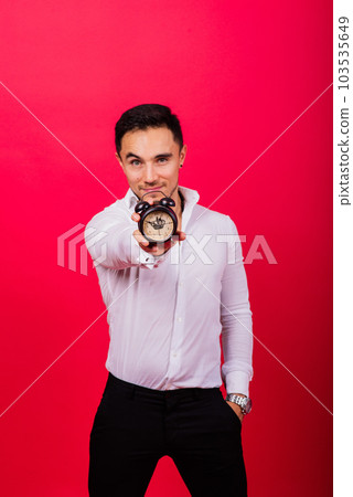 Emotional young man holding clock on red background. Being late concept 103535649