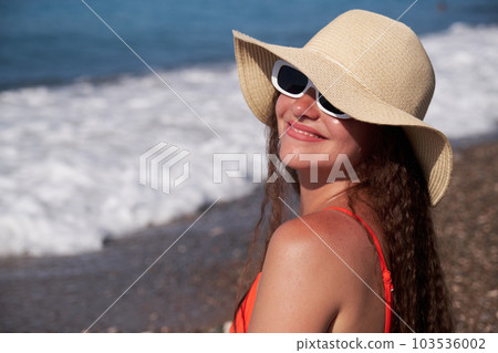 Portrait of a young woman in a hat and glasses on the beach. Looking into the camera. Portrait of a young woman in a hat and glasses on the beach. Looking into the camera. 103536002