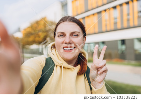 Young caucasian beautiful woman gesturing peace sign on urban background, summer time. Number two. Happy redhead girl take a selfie at vacation. Solo Female Traveler. 103538225