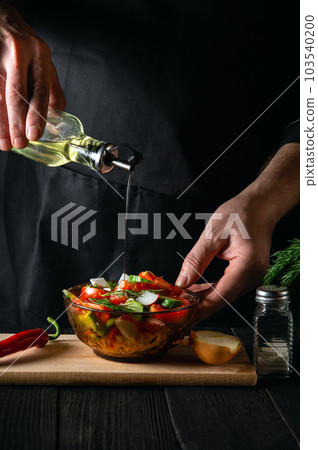 Chef in uniform adding oil to salad from fresh vegetables. The idea of making a diet breakfast or dinner for a restaurant or cafe 103540200