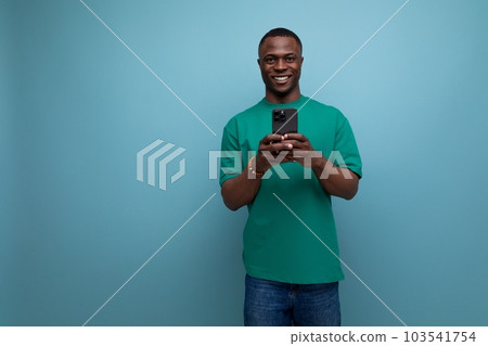 young handsome african guy with a short haircut dressed in a basic t-shirt uses a smartphone to young handsome african guy with a short haircut dressed in a basic t-shirt uses a smartphone to 103541754