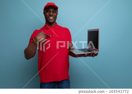 young service engineer american man in a red branded t-shirt and a cap with a laptop young service engineer american man in a red branded t-shirt and a cap with a laptop 103541772