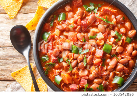 Frijoles charros is a traditional Mexican dish made of pinto beans stewed with onion, garlic, and bacon closeup on the bowl. Horizontal top view Frijoles charros is a traditional Mexican dish made of pinto beans stewed with onion, garlic, and bacon closeup on the bowl. Horizontal top view 103542086