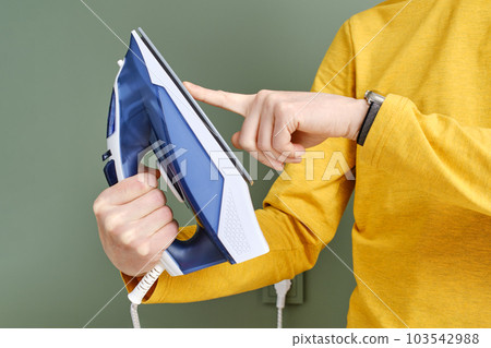Unrecognisable man touching the sole of an iron with finger Unrecognisable man touching the sole of an iron with finger 103542988
