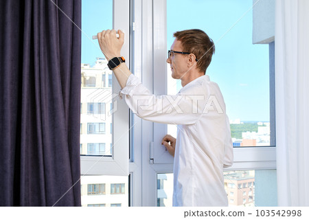 a man stands at open window of high-rise building a man stands at open window of high-rise building 103542998
