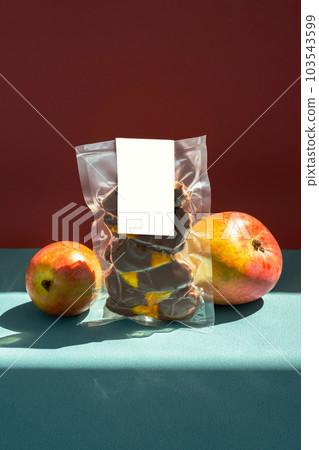 Package of dehydrated mango slices in chocolate. Creative still life of fresh mango and pack of dried fruits. 103543599