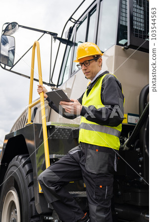 Engineer with tablet computer stands on the stairs to the cab of a truck 103544563