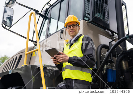 Engineer with tablet computer stands on the stairs to the cab of a truck 103544566