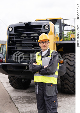 Engineer in a helmet with a digital tablet on the background of construction machine Engineer in a helmet with a digital tablet on the background of construction machine 103544573