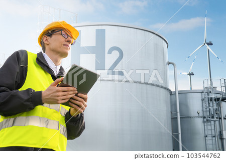 Engineer with tablet computer on a background of green Hydrogen factory. Engineer with tablet computer on a background of green Hydrogen factory. 103544762