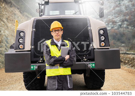 Man worker with tablet computer stands next to mining truck. Man worker with tablet computer stands next to mining truck. 103544783
