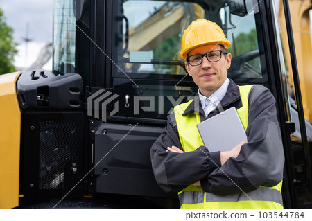 Worker in a helmet with a digital tablet on the background of construction machine. 103544784