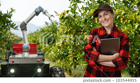 Farmer controls autonomous robot harvester with robotic arm harvesting apples on a smart farm. 103544955