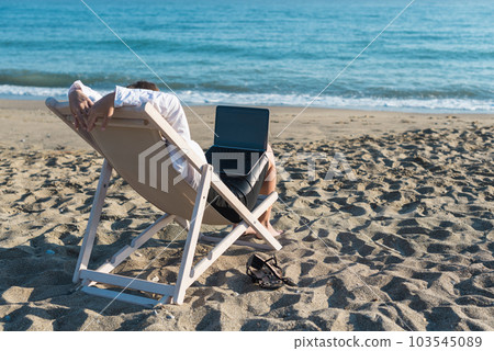 Back view of alone young brunette woman freelancer in office clothes with a laptop looking on the sea sitting on the deck chair on beach. Summer concept Back view of alone young brunette woman freelancer in office clothes with a laptop looking on the sea sitting on the deck chair on beach. Summer concept 103545089