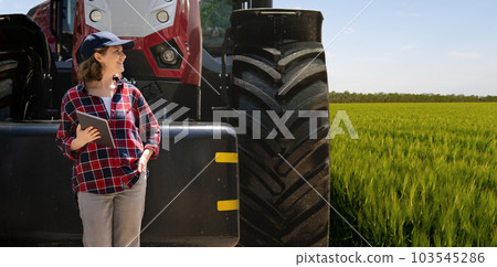 Woman farmer with a digital tablet on the background of tractor 103545286