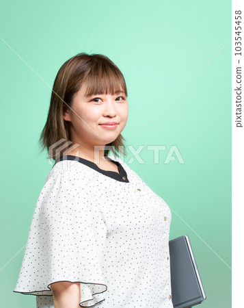 一位年輕女子在她的胳膊下夾著一台平板電腦，商務休閒裝 103545458