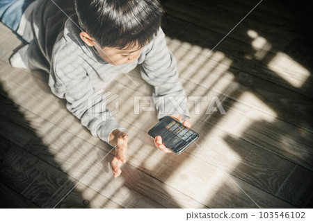 A child touching his parent's smartphone by the window with the shadow of the blinds 103546102