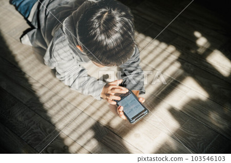 A child touching his parent's smartphone by the window with the shadow of the blinds 103546103