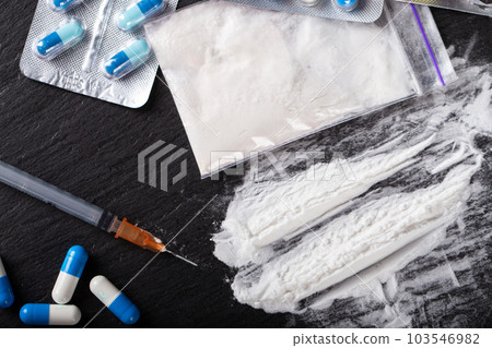 Drugs are scattered on the black table, there is a syringe and pills Drugs are scattered on the black table, there is a syringe and pills 103546982