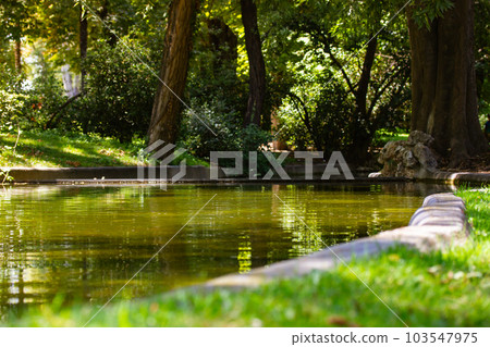 Artificial river pond with a calm surface of water in a green park, forest in spring or summer on a sunny day. Natural backdrop. The concept of ecology, naturalness, tranquility, harmony. Good weather Artificial river pond with a calm surface of water in a green park, forest in spring or summer on a sunny day. Natural backdrop. The concept of ecology, naturalness, tranquility, harmony. Good weather 103547975