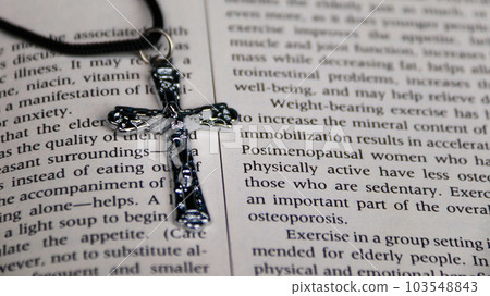 Shiny metal cross with black sling on old book to  recall the kindness of Jesus Christ for all of Christian 103548843