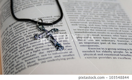 Shiny metal cross with black sling on old book to  recall the kindness of Jesus Christ for all of Christian 103548844
