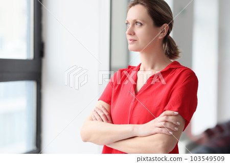 Thoughtful woman with crossed arms stands near window Thoughtful woman with crossed arms stands near window 103549509