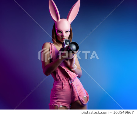 sexy girl in a pink bunny mask with a retro video camera in neon light on the background sexy girl in a pink bunny mask with a retro video camera in neon light on the background 103549667
