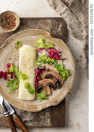 French vegetarian omelet roll filled with cream cheese, green salad and mushrooms for breakfast on rustic wooden board, beige textured background. Top view 103550670