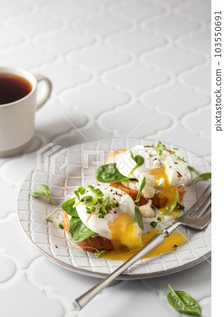 Poached egg sandwich with cream cheese, spinach and micro greens. Healty breakfast bruschetta and morning coffee on white tile background. Keto diet, copy space Poached egg sandwich with cream cheese, spinach and micro greens. Healty breakfast bruschetta and morning coffee on white tile background. Keto diet, copy space 103550691