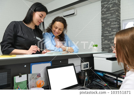 Experienced pleasant young female doctor dentist or beautician aesthetician in black uniform talking to her patient at reception desk, discussing the treatment that need to perform in medical clinic Experienced pleasant young female doctor dentist or beautician aesthetician in black uniform talking to her patient at reception desk, discussing the treatment that need to perform in medical clinic 103551871