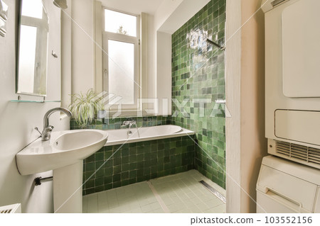 a bathroom with green tiles on the walls and white fixtures in the tub, toilet and sink are all visible a bathroom with green tiles on the walls and white fixtures in the tub, toilet and sink are all visible 103552156