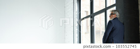 Full length shot of stylish middle aged man in business casual wear and sunglasses leaning on the wall, looking away while posing in loft interior Full length shot of stylish middle aged man in business casual wear and sunglasses leaning on the wall, looking away while posing in loft interior 103552745