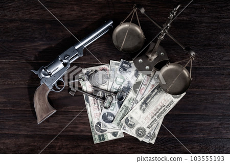 Old west Colt revolver and US banknotes and silver certificates with silver dollar coins and bronze traditional balance scale on wooden table Old west Colt revolver and US banknotes and silver certificates with silver dollar coins and bronze traditional balance scale on wooden table 103555193
