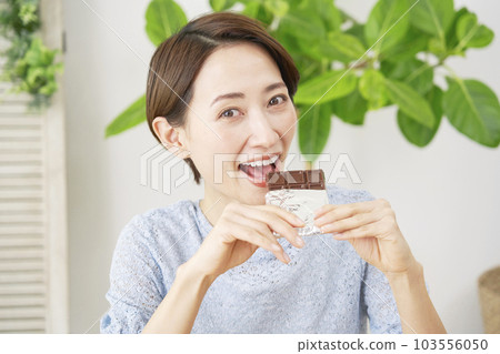 A woman eating a bar of chocolate at home looking at the camera 103556050