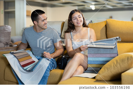 Cheerful couple choosing upholstery for lounge furniture in store Cheerful couple choosing upholstery for lounge furniture in store 103556198