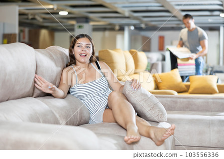 Interested female is testing new sofa in furniture store Interested female is testing new sofa in furniture store 103556336
