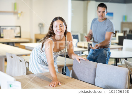 Wife feels surface of countertop with hand,husband dissuades from chosen table model 103556368