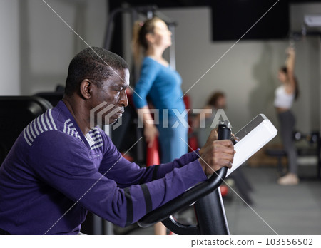 African man using exercise bicycle in gym 103556502
