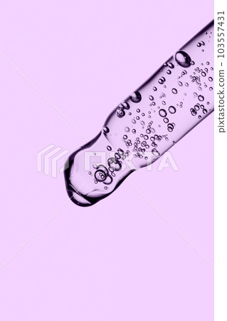 Transparent pipette with cosmetics on a purple background. Transparent pipette with cosmetics on a purple background. 103557431