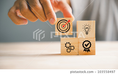 Wood block stacking arranged by a businessman's hand, signifying a business strategy and Action plan. The image showcases the concept of product development and marketing. 103558497