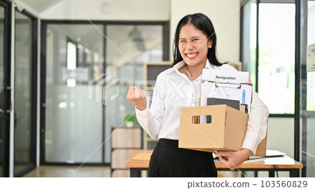 Smiling Asian female office worker is celebrating her resignation, carrying her personal stuff Smiling Asian female office worker is celebrating her resignation, carrying her personal stuff 103560829