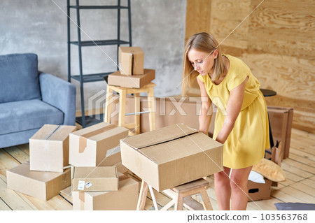 Young girl packing plates into the boxes ready to move. Woman unpacking moving boxes in her new home. unpack personal stuff from carton boxes. Young girl packing plates into the boxes ready to move. Woman unpacking moving boxes in her new home. unpack personal stuff from carton boxes. 103563768