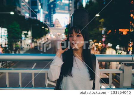 A young woman standing with a guitar and a smartphone 103564040